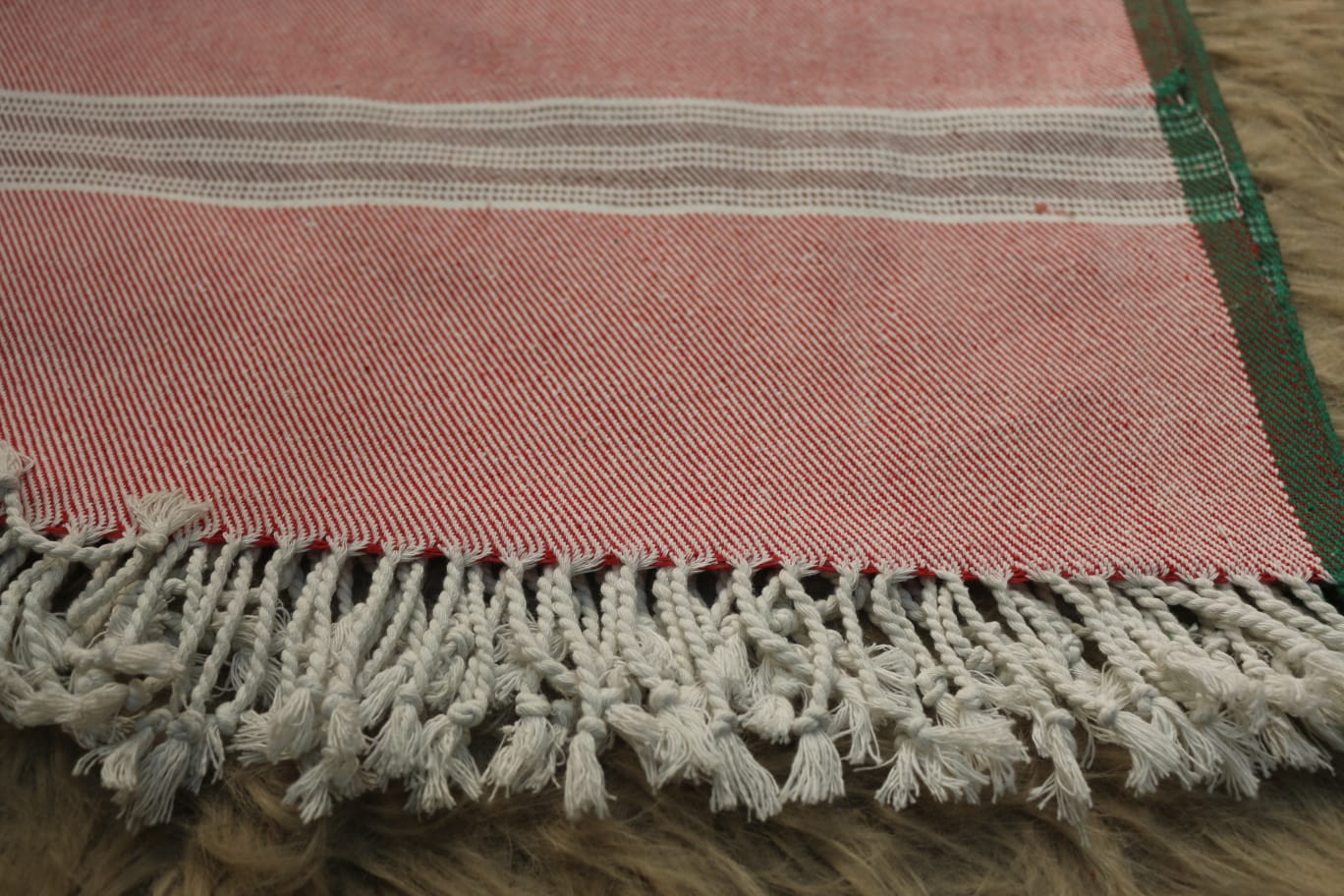 Close-up of a pink woven rug with white fringe on a wooden floor.