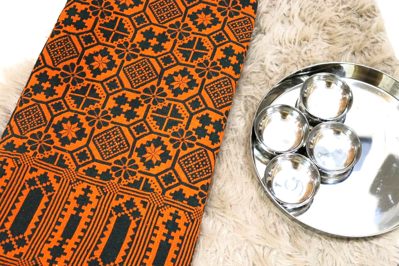 Orange fabric with black geometric patterns next to a silver tray with round items on a beige surface
