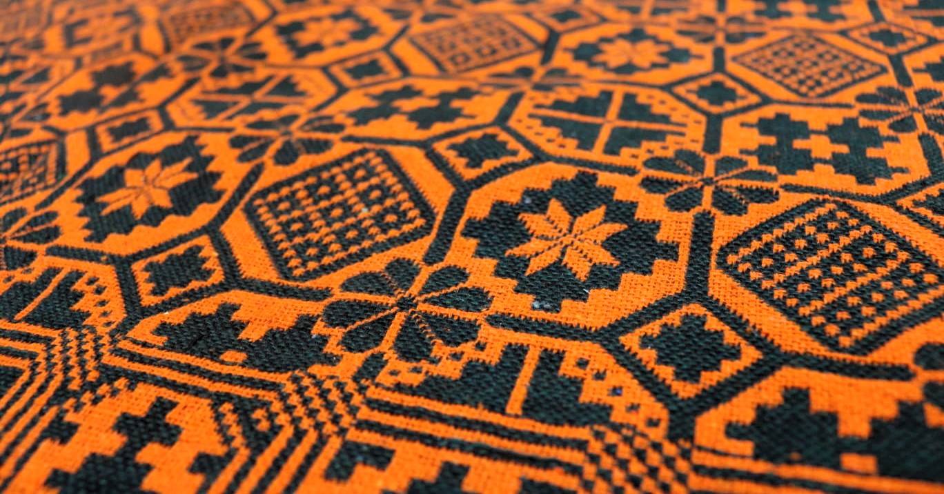 Close-up of a patterned khes fabric with green geometric designs on an orange background