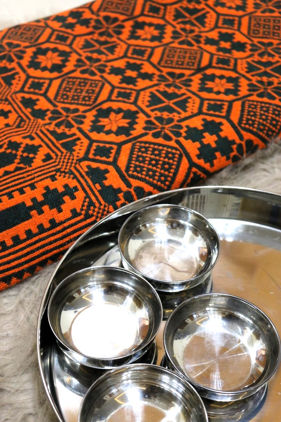 Set of stainless steel bowls on a metal tray with an orange and black patterned khes fabric in the background.