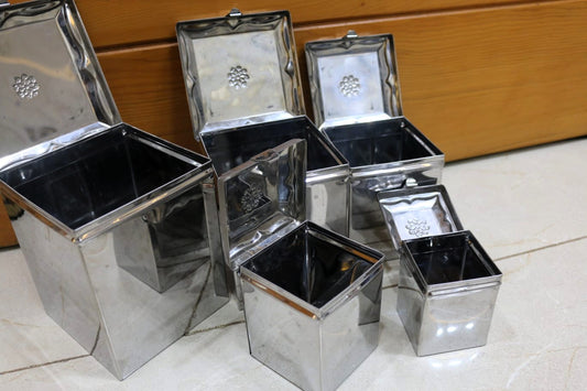 Set of metallic storage boxes with lids on a tiled floor.