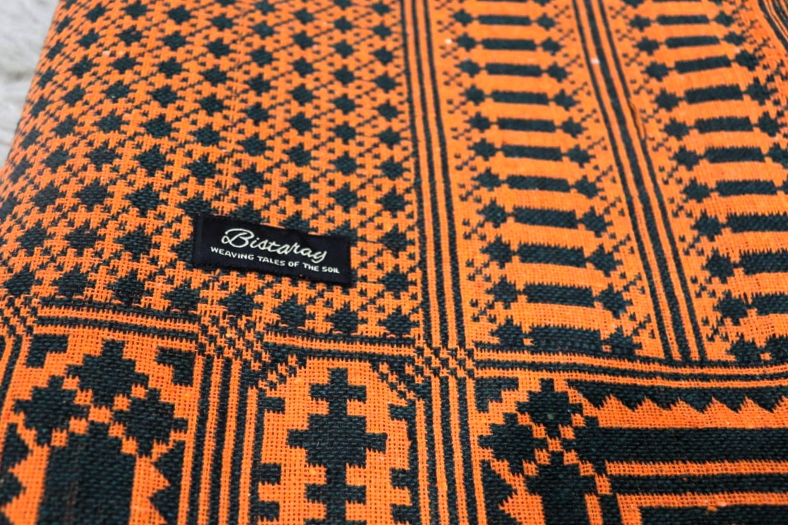 Close-up of a patterned khes fabric with orange and black design, featuring a brand label.