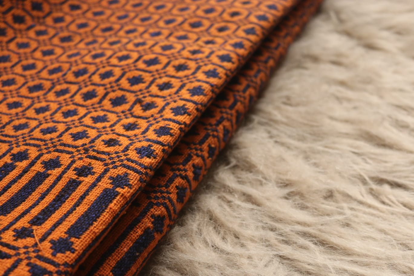 Orange fabric with black geometric pattern on a textured beige surface