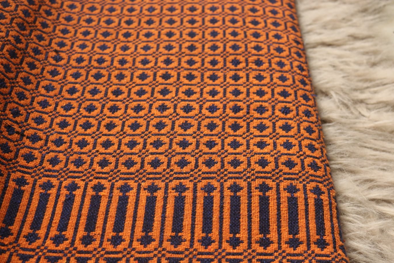 Close-up of a patterned fabric with orange and black design on a textured surface.