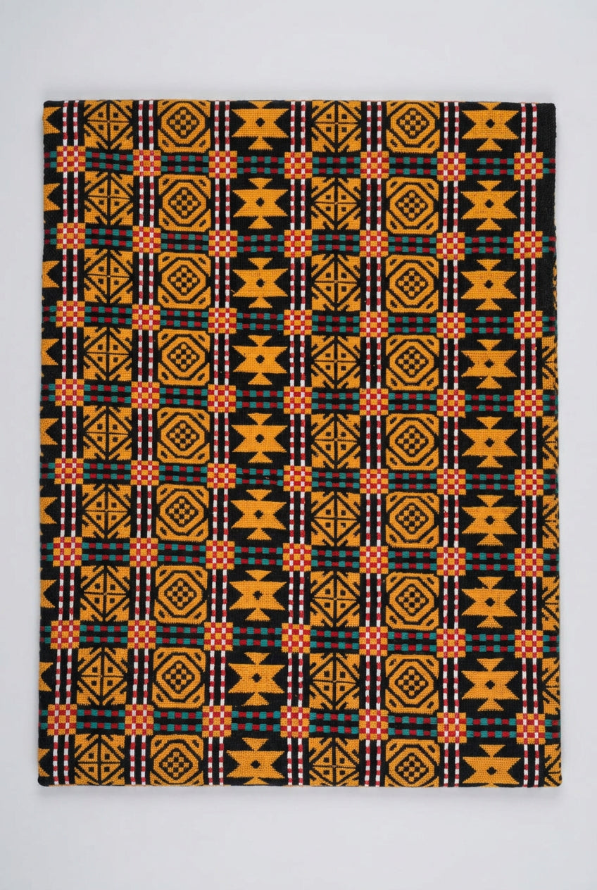 A close-up of a woven textile with a bold geometric pattern in yellow, black, red, white, and teal, laid flat on a light surface.